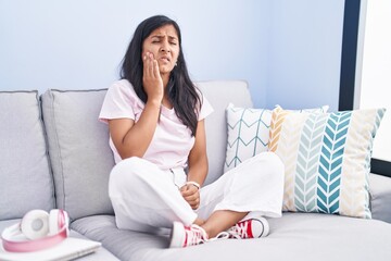 Sticker - Young hispanic woman sitting on the sofa at home touching mouth with hand with painful expression because of toothache or dental illness on teeth. dentist