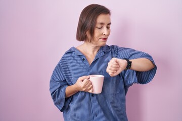 Poster - Middle age hispanic woman drinking a cup coffee checking the time on wrist watch, relaxed and confident