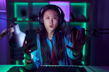 Canvas Print - Young asian woman playing video games with smartphone doing stop gesture with hands palms, angry and frustration expression