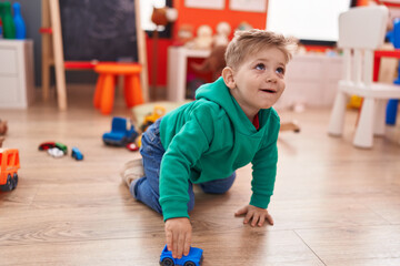 Wall Mural - Adorable caucasian boy playing with car toy sitting on floor at kindergarten