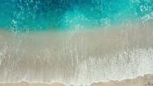 Aerial Top View Of Ocean Turquoise Blue Waves Break On A Beach. Aerial Shot Of Beach With Small Stones Meeting Ocean Water And Foam. Top View Of Paradise Island. Tidal Wave Floods Sandy Beach. Relax.