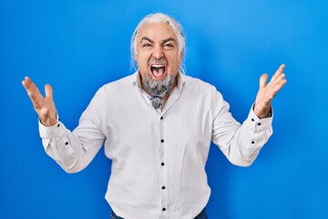 Sticker - Middle age man with grey hair standing over blue background crazy and mad shouting and yelling with aggressive expression and arms raised. frustration concept.