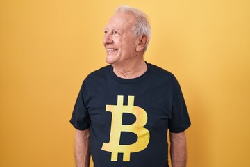 Poster - Senior man with grey hair wearing bitcoin t shirt looking away to side with smile on face, natural expression. laughing confident.