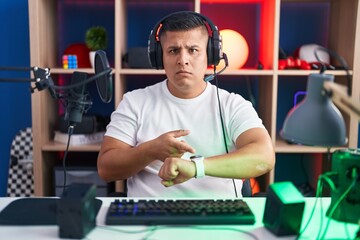 Sticker - Young hispanic man playing video games in hurry pointing to watch time, impatience, upset and angry for deadline delay