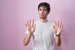 Young hispanic man standing over pink background moving away hands palms showing refusal and denial with afraid and disgusting expression. stop and forbidden.