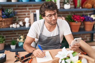 Canvas Print - Young hispanic man florist using smartphone writing on notebook at flower shop