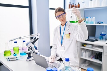 Poster - Young caucasian woman scientist holding test tube using laptop at laboratory