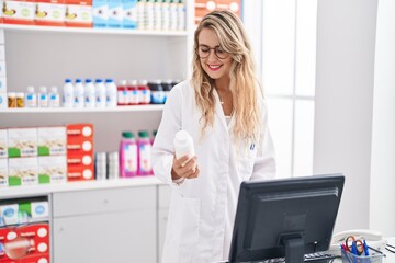 Wall Mural - Young woman pharmacist holding pills bottle working at pharmacy