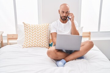 Sticker - Young bald man using laptop talking on smartphone at bedroom