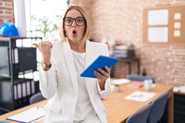 Canvas Print - Young caucasian woman working at the office wearing glasses surprised pointing with hand finger to the side, open mouth amazed expression.