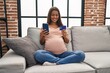 © Krakenimages.com - Young latin woman pregnant using smartphone and credit card at home