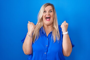 Poster - Caucasian plus size woman standing over blue background celebrating surprised and amazed for success with arms raised and open eyes. winner concept.