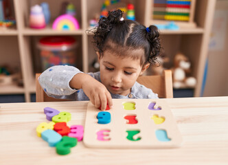 Adorable hispanic girl playing with maths puzzle game sitting on table at kindergarten