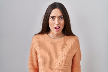 Poster - Young brunette woman standing over white background afraid and shocked with surprise and amazed expression, fear and excited face.