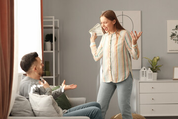 Wall Mural - Angry young woman with money shouting at her husband at home. Domestic violence concept