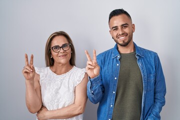 Poster - Hispanic mother and son standing together smiling with happy face winking at the camera doing victory sign with fingers. number two.