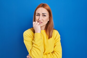 Sticker - Young woman standing over blue background looking stressed and nervous with hands on mouth biting nails. anxiety problem.