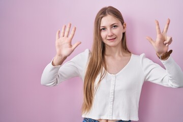 Canvas Print - Young caucasian woman standing over pink background showing and pointing up with fingers number eight while smiling confident and happy.