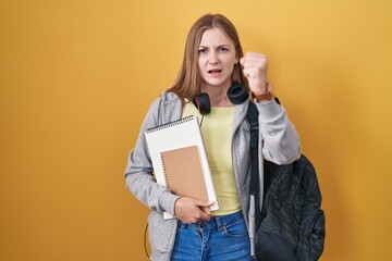 Canvas Print - Young caucasian woman wearing student backpack and holding books angry and mad raising fist frustrated and furious while shouting with anger. rage and aggressive concept.