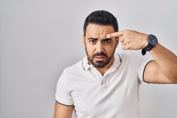 Sticker - Young hispanic man with beard wearing casual clothes over white background pointing unhappy to pimple on forehead, ugly infection of blackhead. acne and skin problem