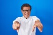 © Krakenimages.com - Middle age hispanic man standing over blue background pointing to you and the camera with fingers, smiling positive and cheerful