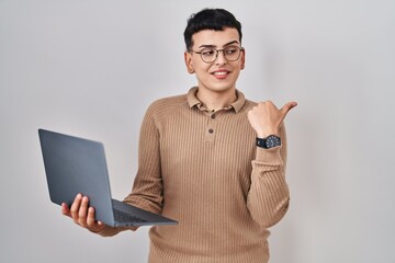 Poster - Non binary person using computer laptop smiling with happy face looking and pointing to the side with thumb up.