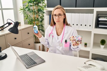 Wall Mural - Young blonde doctor woman holding glucometer and sweets skeptic and nervous, frowning upset because of problem. negative person.