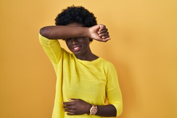 Poster - African young woman standing over yellow studio covering eyes with arm smiling cheerful and funny. blind concept.