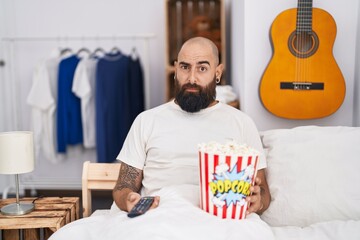 Canvas Print - Young hispanic man with beard and tattoos eating popcorn in the bed skeptic and nervous, frowning upset because of problem. negative person.