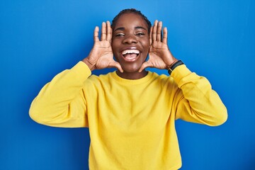 Beautiful black woman standing over blue background smiling cheerful playing peek a boo with hands showing face. surprised and exited