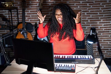 Poster - Plus size hispanic woman playing piano at music studio celebrating crazy and amazed for success with arms raised and open eyes screaming excited. winner concept