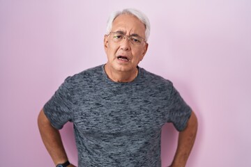 Poster - Middle age man with grey hair standing over pink background in shock face, looking skeptical and sarcastic, surprised with open mouth