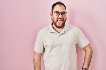 Wall Mural - Plus size hispanic man with beard standing over pink background sticking tongue out happy with funny expression. emotion concept.