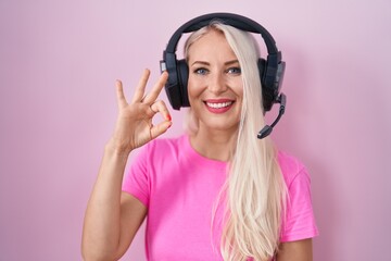 Wall Mural - Caucasian woman listening to music using headphones smiling positive doing ok sign with hand and fingers. successful expression.