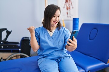 Sticker - Hispanic girl with down syndrome working at physiotherapy using smartphone pointing thumb up to the side smiling happy with open mouth