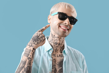 Wall Mural - Tattooed man with sunscreen cream on his face against light blue background