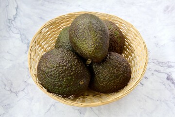 Wall Mural - Top view of a wooden basket with avocados on a marble table