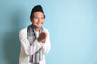 Portrait of Asian muslim man in white koko shirt with skullcap showing apologize and welcome hand gesture. Isolated image on blue background