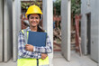 © Supachai - Asian woman engineer holding document smiling at construction site. Confident female Indian wearing protective helmet and vest working in factory making precast concrete wall for real estate housing.