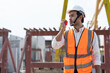 © Supachai - Portrait of male civil engineer wearing safety vest with white helmet holding walkie talkie talking with worker at factory making precast concrete wall.