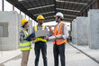 © Supachai - Team of construction engineers wearing vest and helmet safety discussing project at construction site. Group Indian foreman with laptop, paperwork working at factory making precast concrete wall.
