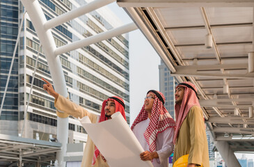 Teamwork of happy Arab businessman standing holding blueprint with meeting and talking at construction site in city.