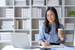 © amnaj - Happy young asian businesswoman sitting working at office and drinking coffee.