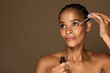 Beautiful black middle aged woman using nourishing face serum after shower, enjoying organic beauty product