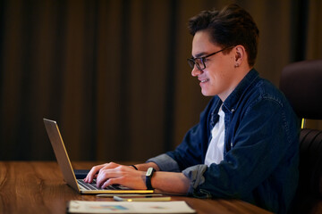 Aufkleber - Side view of positive young guy typing on laptop keyboard