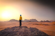 Wadi Rum w Jordanii. Mężczyzna stojący na pustynnej formacji skalnej patrzący na wschód słońca. 