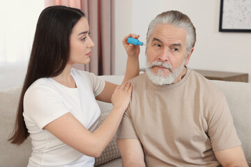 Canvas Print - Young woman dripping medication into man's ear at home