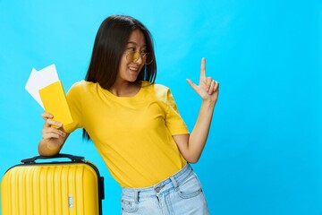 Wall Mural - Asian woman traveling with yellow suitcase and tickets with passport in hand, tourist traveling by plane and train with luggage on blue background