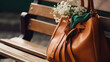 Female leather handbag with a tied scarf on the bench. Brown purse with a bouquet of white spring flowers