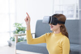 Fototapeta Sypialnia - Surprised Young latin or asian woman in VR headset touching air, Smiling white woman wearing vr glasses while sitting on sofa at home.